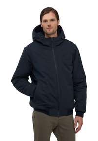 Giacca a vento navy con cappuccio, apertura con zip, due tasche laterali, polsini e orlo a costine, realizzata in un tessuto liscio con design minimalista.