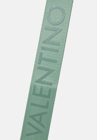 Cintura in stoffa intrecciata verde con la parola "VALENTINO" stampata in grandi lettere maiuscole lungo la sua lunghezza.