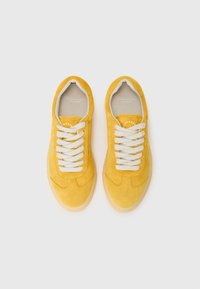 Sneaker gialle in suede con lacci bianchi, punta tonda e suola in gomma leggera. Presentano un marchio sul lato interno e una texture liscia.