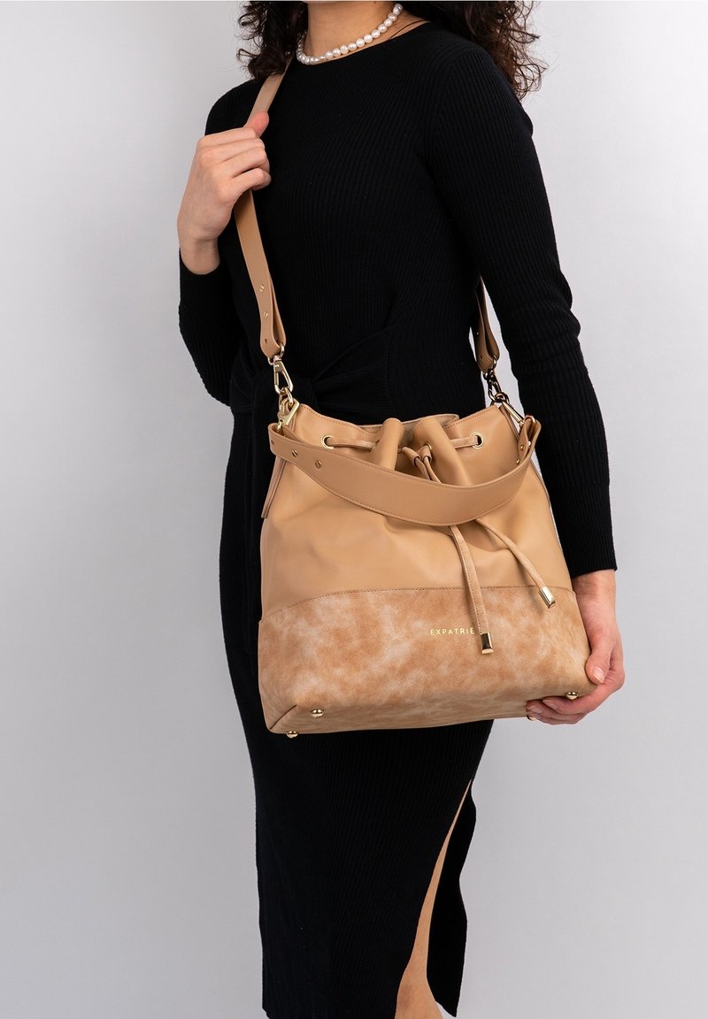 Sac seau en cuir camel avec base en daim, fermeture à cordon et garniture dorée. Bandoulière réglable et détail de logo à l'avant.