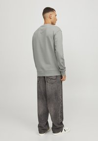 Sudadera gris con puños de canalé, combinada con jeans negros de corte holgado. El conjunto presenta una silueta relajada y un diseño sencillo.