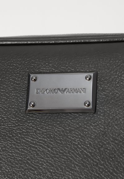 Suurendatud vaade musta kivitootelisest nahapindast, millel on ristkülikukujuline metallplaat, millel on graveeritud "EMPORIO ARMANI."
