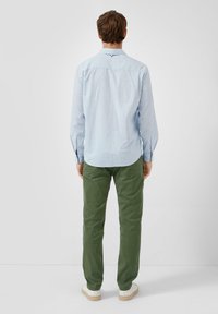 Jasnoniebieska koszula zapinana na guziki, wykonana z bawełny, w zestawieniu z ciemnozielonymi spodniami chino i białymi trampkami, pokazana od tyłu.