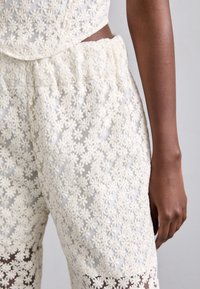 Hvite broderte shorts med teksturerte blomsterdesign og elastisk midje. Stoffet ser lett og litt gjennomsiktig ut.