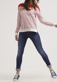 Rood-wit gestreepte trui met een effen rode schouderontwerp, gecombineerd met donkerblauwe skinny jeans die bij de enkels zijn opgerold en zwarte sneakers.