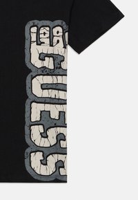 Crna majica s kratkim rukavima koja prikazuje dio izrezbarenog bijelog i sivog grafičkog dizajna s blokovskim velikim slovima.