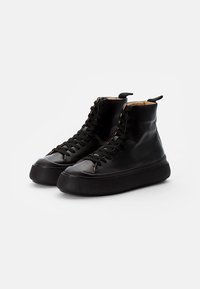 Czarne skórzane sneakersy typu high-top z teksturowaną, grubą gumową podeszwą, wyposażone w metalowe oczka i czarne sznurówki. Obecny subtelny detal w postaci przeszyć.