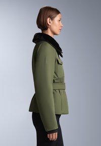 Olivno zelena jakna z črnim umetnim krznom, strukturirana zasnova, pasovi v pasu in žepki na obeh straneh. Gladko blago in krojena silhueta.