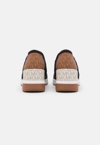 Baskets noires avec un talon texturé marron et beige clair. Motif de logo notable sur le talon, semelle intermédiaire blanche et semelle extérieure en caoutchouc marron.