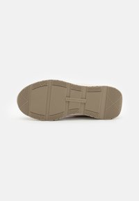 Beige színű gumitalp, mely texturált tapadási mintázattal rendelkezik, és jól látható vízszintes és függőleges hornyok találhatók rajta a tapadás érdekében. A márkajelzés a középpontban látható.