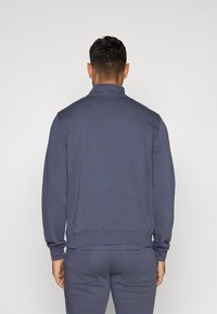 Dark blue, long-sleeve pullover with a high collar. Smooth fabric, ribbed cuffs and hem. Features minimal back design and fitted style.