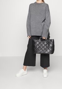 Gequilted zwarte leren handtas met een vierkante handgreep, gecombineerd met een grijze gebreide trui en zwarte wijde broek, aangevuld met witte sneakers.