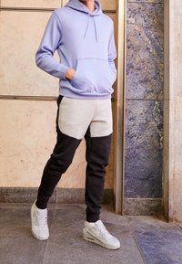 Ljuslila huva-tröja med en framficka, parat med grå och svart färgblockerade joggers och ljusgråa träningssneakers.