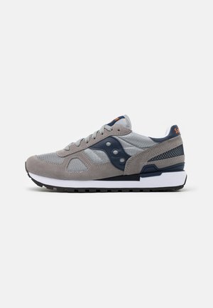 Scarpa sportiva grigia con una combinazione di materiali in suede e mesh; presenta dettagli blu navy, chiusura con lacci e una suola intermedia bianca.