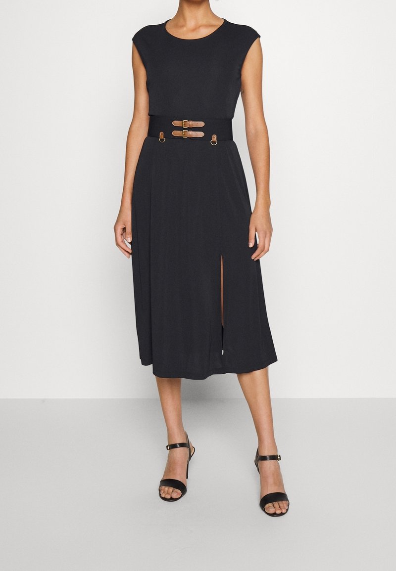 Černé šaty po kolena s přiléhavým korzetem, krátkými rukávy a páskem v pase s dvěma hnědými popruhy. Obsahují boční rozparek pro snadnější pohyb.