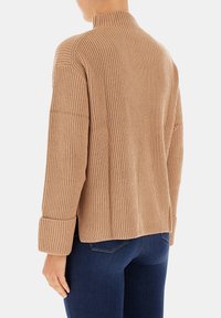 Maglione beige a coste con collo alto e maniche lunghe, caratterizzato da polsini arrotolati e una vestibilità morbida, mostrato da dietro.