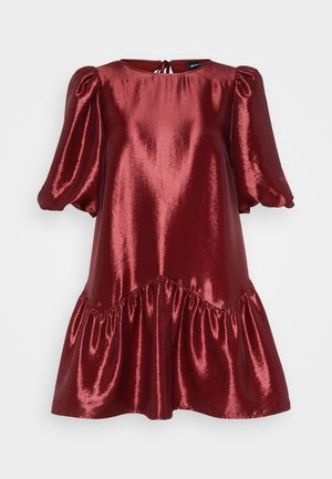 Rdeča metalna obleka s napihnjenimi rokavi, okroglem izrezu in nabranim robom. Gladka tekstura z lesketajočo se površino. Zavezuje se na hrbtu.