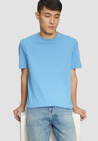 Svetlomodré bavlnené tričko s okrúhlym výstrihom a krátkymi rukávmi, v kombinácii s uvoľnenými džínsami svetlého prania, umiestnené na neutrálnom pozadí.