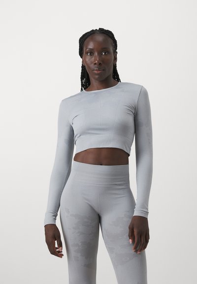 Light gray athletic crop top with long sleeves and fitted waistband, paired with high-waisted leggings featuring a subtle pattern.