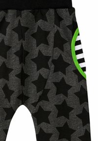 Pantaloni jogger in tessuto grigio con motivo a stelle nere, dotati di una tasca con rifiniture verdi e strisce in bianco e nero. Vita elasticizzata per il massimo comfort.