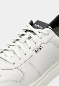White leather sneaker with white laces and "BOSS" branding on the side and black heel tab against a plain background.