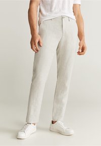 Lichtgrijze linnen broek met een rechte pasvorm, voorzien van een knoopsluiting en zijzakken, gecombineerd met witte sneakers.