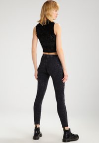 Čierny zamatový crop top v kombinácii s čiernymi textúrovanými legínami, ktoré majú priliehavý strih a elastický pás, nosený s čiernymi kotníkmi.