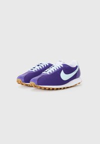 Paarse sportieve schoenen met witte veters en een lichtblauwe swoosh; bovenkant van mesh, rubberen buitenzool met een gestructureerde grip.