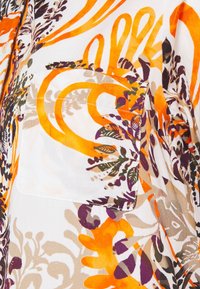 Valkoinen kangas, johon on ommeltu tasku, jossa on oranssin, violetin, beigen ja vihreän abstrakti kukkakuosi.