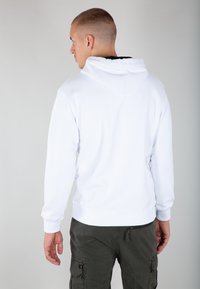 Sudadera blanca con una gran capucha y puños acanalados, combinada con pantalones cargo verdes oscuros que tienen bolsillos laterales y un detalle con cremallera.