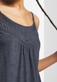 Námořnická modrá tílko s krajkovými detaily, s výstřihem ve tvaru lodi a plisé texturou. Vyrobeno z měkkého materiálu, ideální pro každodenní nošení.