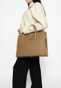 Borsa in pelle color cuoio con design strutturato, manici superiori e pattina frontale. Presenta cuciture a contrasto e piedini protettivi alla base.