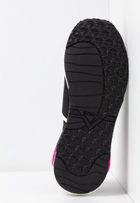 Mustan urheilujalkineen pohja, jossa on teksturoitu kumipohja, pinkit yksityiskohdat, valkoinen raita ja logoyksityiskohtia. Suunniteltu tarjoamaan pitoa ja tukea.