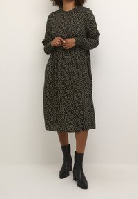 Robe noire et blanche à motifs avec une coupe décontractée, manches longues et encolure ronde, associée à des bottines noires.