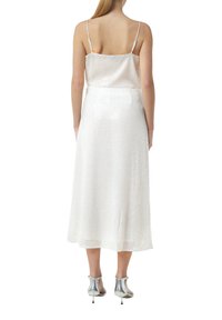 Weißes, schimmerndes Midi-Kleid mit dünnen Spaghettiträgern, einer fließenden Silhouette und einem leicht strukturierten Stoff. Kombiniert mit silbernen High Heels.