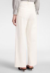 Pantaloni bianchi a gamba larga realizzati in misto cotone, con vita alta, cinque tasche e una texture liscia. Abbinati a sandali con tacco scuro.