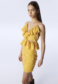 Vestido amarillo con escote con volantes y cintura tipo peplum, que presenta una falda ajustada y fruncida. Tela suave con una textura agradable y tirantes ajustables.