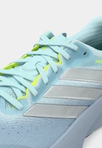 Αθλητικό παπούτσι ανοιχτού γαλάζιου χρώματος με υφασμάτινο επάνω μέρος με υφή, γκρι τρεις ρίγες, νέον πράσινες λεπτομέρειες και επίπεδα κορδόνια. Μαλακή, επενδεδυμένη σόλα.