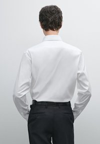 White dress shirt with long sleeves, featuring a straight cut and smooth texture, paired with dark trousers and a black belt.