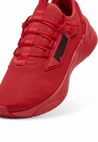 Zapatilla deportiva roja con parte superior de malla y suela de goma reforzada. Presenta cordones y un logo negro de PUMA en el costado. Diseño de punta redondeada.