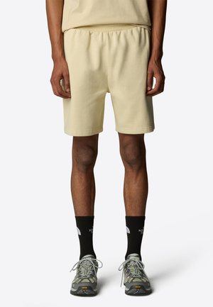 Yellow cotton blend shorts with an elastic waistband, side pockets, and a relaxed fit. Black crew socks and hiking shoes complete the outfit.