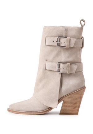 Light beige suede ankle boot with pointed toe, two adjustable straps with metal buckles, and stacked wooden block heel.