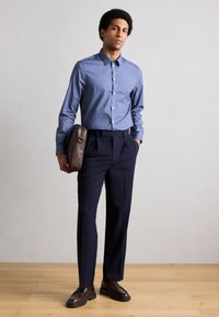 Šviesiai mėlynos spalvos marškiniai su sagomis, derinami su tamsiai mėlynais klostuotais kelnėmis. Išvaizdą papildo ruda odinė pašto karjero tipo rankinė ir rudi mokasinai.