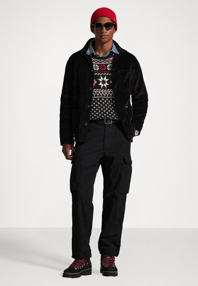 Black corduroy jacket, patterned knit sweater, black cargo pants, red knit beanie, and black hiking boots with red laces. Sunglasses worn.