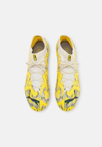 Botas de fútbol amarillas brillantes con una superficie texturizada, que presentan acentos en gris y negro. La parte superior de punto y los cordones en contraste completan el diseño.