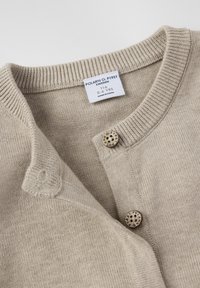 Beige gestrickte Kinderjacke mit geripptem Kragen, zwei Holzknöpfen, die mit "POLARN O. PYRET" graviert sind, und Größenetikett 116 für 5-6 Jahre.