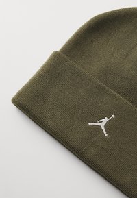 Berretto in maglia verde oliva con una texture morbida, caratterizzato da un logo Jumpman ricamato in bianco sul davanti. Risvolto nella parte inferiore.