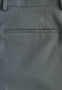 Pantalones grises a medida con una tela suave, un bolsillo trasero con cierre plano y costuras precisas a lo largo de las costuras.