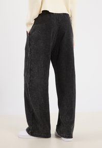 Zwart denim broek met wijde pijpen en een vervaagde textuur, zijzakken en een casual pasvorm, gecombineerd met witte sneakers.