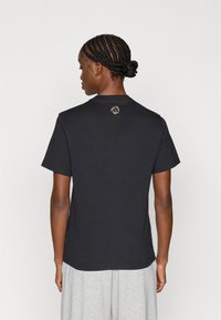 Črna kratkohlačasta majica iz bombaža, z okroglim ovratnikom in majhnim logotipom na zgornjem hrbtu. Gladka tekstura.